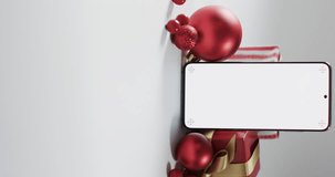 Vertical video of christmas red baubles, presents and smartphone with copy space on white background. Christmas, decorations, tradition and celebration concept.