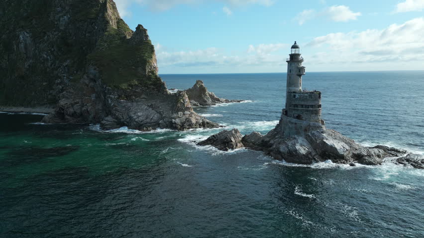 Top view of rocks in sea with abandoned lighthouse. Clip. Beautiful view of old lighthouse and rocky cape in sea. Landscape lighthouse on rocky cape in ocean on sunny summer day