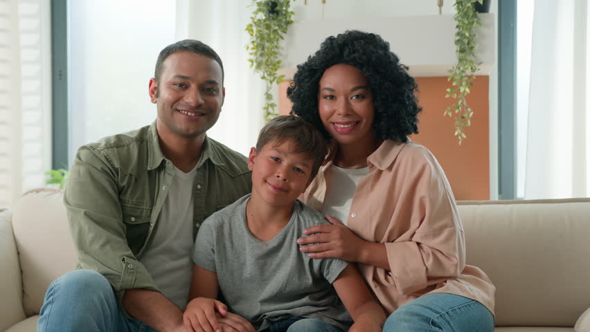 Multiracial African American Caucasian happy family portrait at home smiling parents father and mother hug little boy child preschool kid on sofa couch diverse generation parenthood love children care Royalty-Free Stock Footage #1109925617
