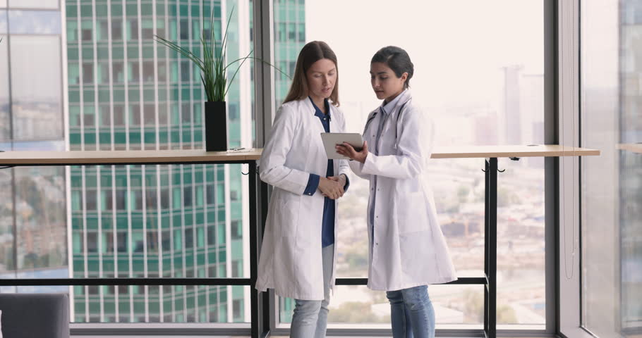 Multiracial women doctors discuss patient health check up, treatment plan while walking along clinic hallway, share opinion with colleague engaged in teamwork and workflow use tablet. Medicine, tech Royalty-Free Stock Footage #1109931127