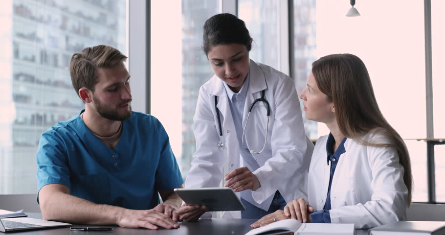 Female general practitioner talks to colleagues, provide help, assist with new medical app software use tablet, discuss patient disease treatment plan gathered in office. Cooperation, tech, medicare Royalty-Free Stock Footage #1109931133