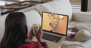 Biracial woman using laptop on couch at home online shopping for stationery, slow motion. Retail business, sale, communication and digital interface digitally generated video.