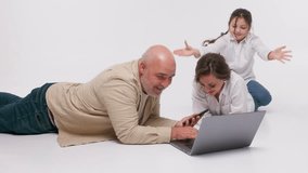 Happy bearded man with his wife and schoolgirl daughter watching a funny video on the computer. Family playing games on a laptop or shopping in an online store on an isolated light background.