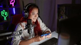 Happy redhead gamer girl, young streamer's night of fun, playing video games on her phone in a cozy gaming room, confidently streaming with bright smiles