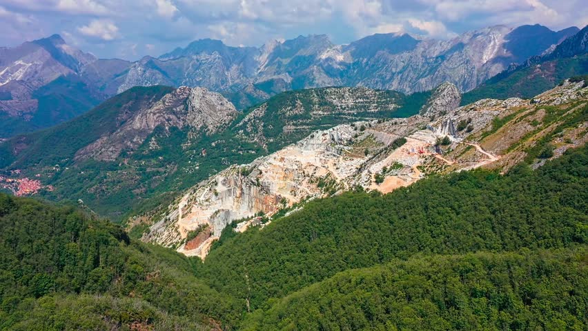 Slow aerial backwards revealing shot of marble quarry in Apuan Alps, Carrara, Italy. Drone shot on sunny day, famous white Carrara marble excavated since Ancient Rome, used for many masterpieces, open