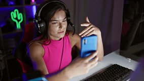 Captivating glimpse of a young hispanic woman streamer smiling, immersed in a lively video call on her smartphone, lighting up the gaming room at home late in the night.