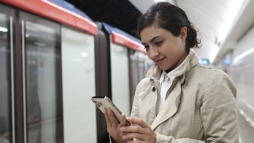 Happy woman standing at metro station. Girl using smartphone internet surfing, communication online. Businesswoman holding phone checking news. Public transport. Browsing social networks site. 4K | Shutterstock HD Video #1109947611
