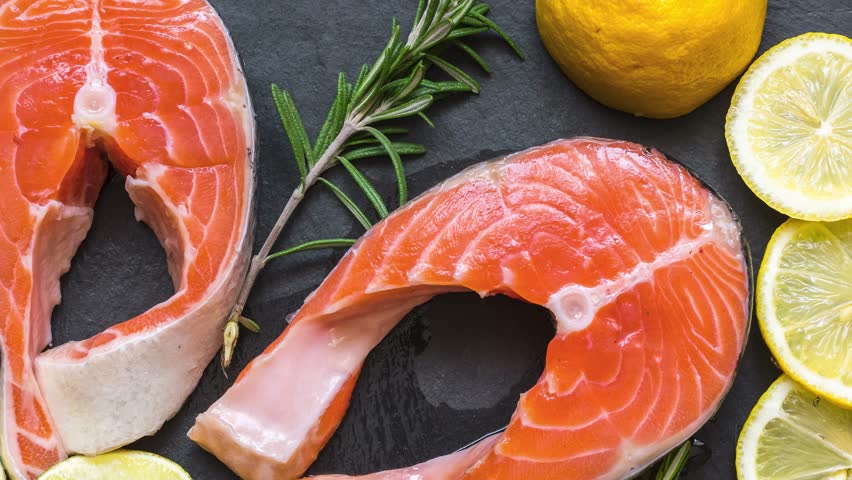 Salmon steaks with rosemary and lemon on black slate board on wooden table. Fish rich in omega 3 fatty acid. Healthy and diet seafood. Keto and low carb food. Top view