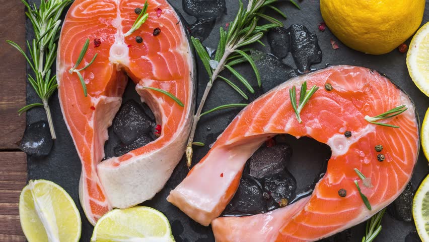 Salmon steaks, fish rich in omega 3, with rosemary and lemon on black slate board. Healthy and diet seafood. Keto and low carb food. Top view