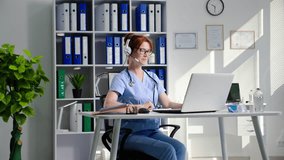 beautiful young female doctor consults patients using headset and video communication on computer while receiving patients online while sitting in a medical office
