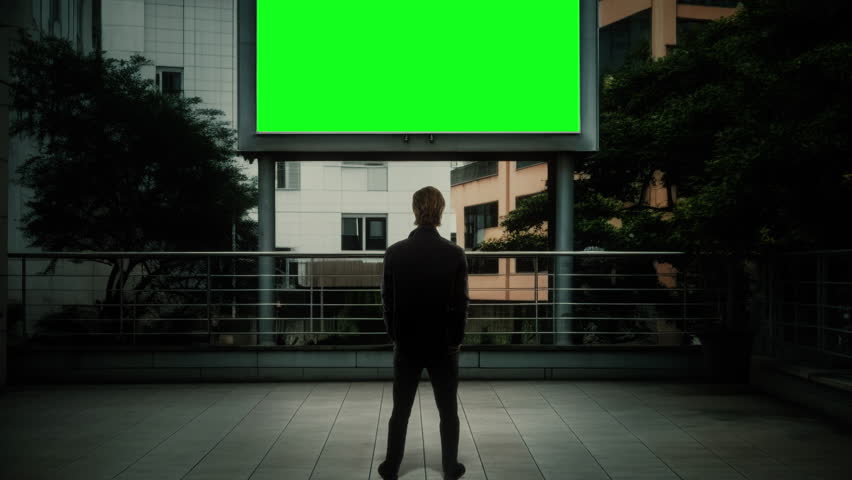 Billboard Green Screen Man Looking Outdoor Panel Tilt Up. Man standing in front of an exterior green screen billboard stand, tilt up Royalty-Free Stock Footage #1109956951