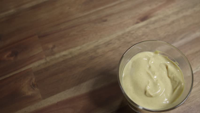 Medium close shot of yellow mustard sitting in a small glass jar. Top shot, panning. Nobody, studio.