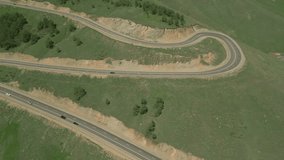 A steep serpentine road between rocky hills in Lori, Armenia. On the highway are cars and trucks. There is grass and trees growing on the mountains. Drone video. Side view, flying sideways with a turn