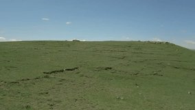 Drone video. A sideways flyby along a green stony hill, from behind which appears a highway with cars, a small village and the high snowy mountain Aragats. Lori region, Armenia.