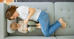 Woman and her little son lying on cozy sofa with smartphone, above view.