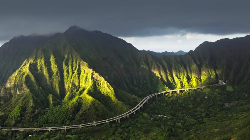 Main road of Oahu island with breathtaking landscape at sunny sunrise with beautiful golden light shining on green mountain. Aerial mountain tunnel in Interstate H3, most expensive highway in USA 4K Royalty-Free Stock Footage #1109969481