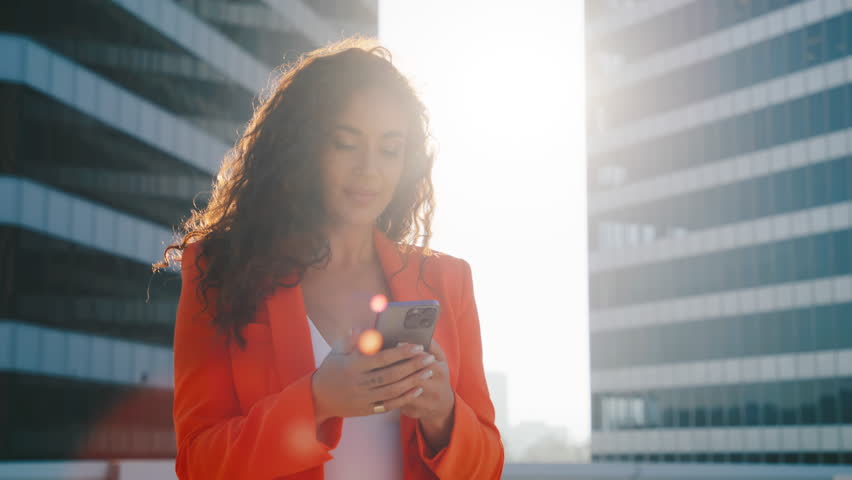 Cheerful gorgeous latina woman celebrating online victory standing in urban downtown in sunset golden light. Multi racial holds cellphone check e-mail app feel excited, looking happy by lottery win 4K Royalty-Free Stock Footage #1109969489
