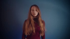 Portrait of a young beautiful artistically refusing pretty caucasian girl with long brown hair in a burgundy sweater looking at the camera and shaking her head from side to side on a blue background