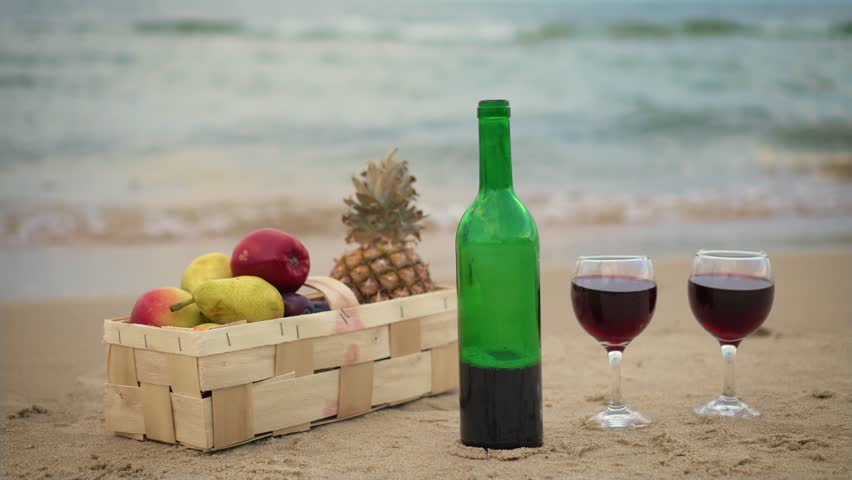 Closeup of summer picnic basket with fresh fruits, wine bottle with glasses near ocean. Picnic at seashore during summer evening