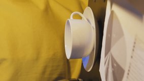 Vertical video. Close-up of man pouring coffee while working overtime, spilling coffee over the rim of cup while sitting at desk in night office