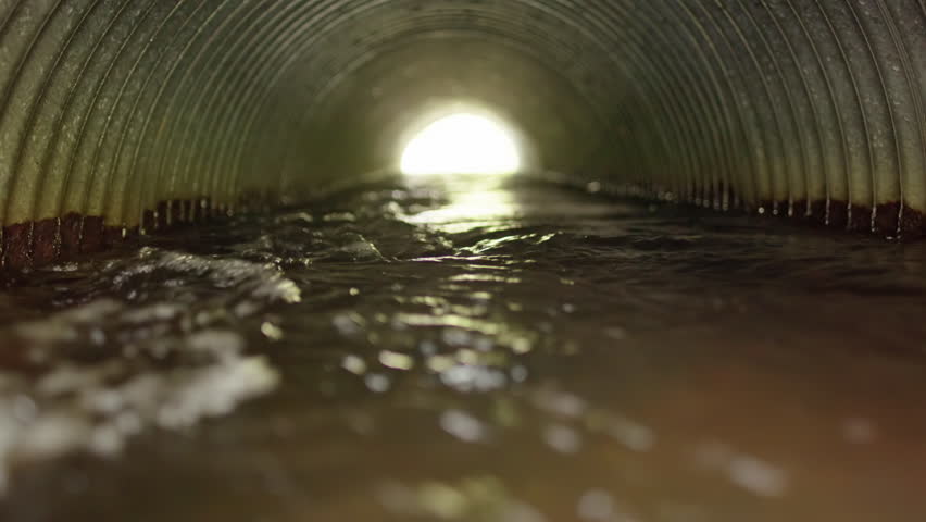 Flood water running through corrugated pipe with light at end, zoom shot