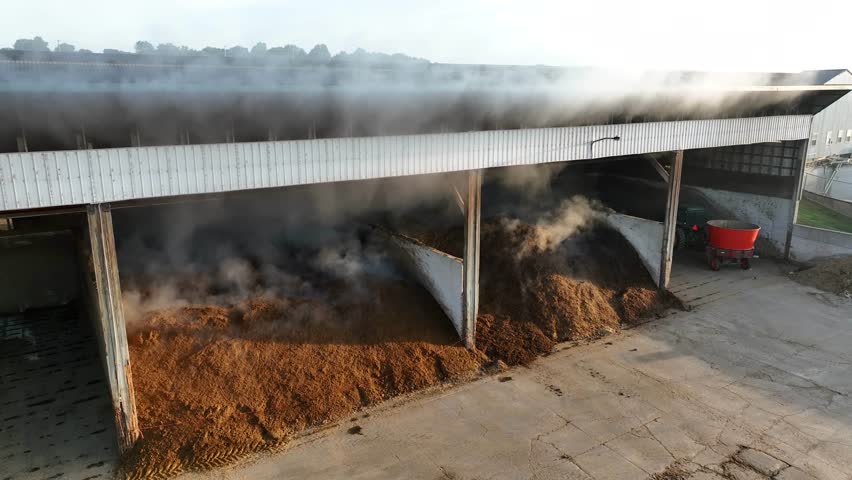 Silage producing steam in barn. Aerial rising shot into smoke during cold morning sunrise on American farm. Royalty-Free Stock Footage #1109974509