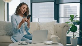 Online shopping concept. Super excited young woman using smart phone surfing social media, making online purchases sitting on sofa. Stylish lady spending time at home with cell gadget technology 4K