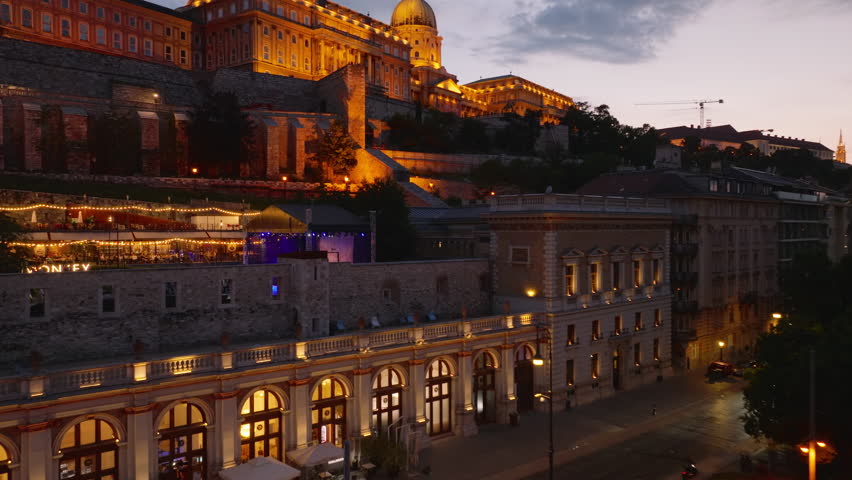 Aerial ascending footage of Buda Castle on hill. Illuminated sight at dusk. Revealing urban neighborhood and twilight sky. Budapest, Hungary
