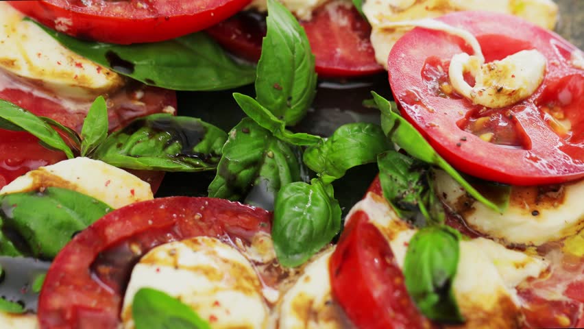 Italian Caprese Salad with sliced tomatoes, mozzarella cheese and basil on dark background. Close up