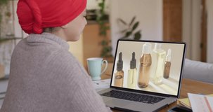 Biracial woman at table using laptop, online shopping for beauty products, slow motion. Retail business, sale, communication and digital interface digitally generated video.
