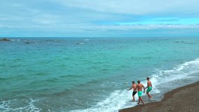 Top view of people running into sea. Clip. Men run to swim in blue sea on background of cloudy horizon. Men run to swim on coast of beautiful sea with reefs