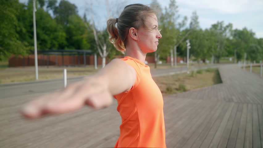 Close-up of a beautiful young girl doing yoga exercises in the park on a summer sunny morning. In the background paths made of wood and a green array of trees