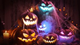 Many Halloween Jack-o'-lanterns in spider web and garlands lie on doorstep of house. Zooming out tracking shot of brightly colored carved pumpkins with eerie faces glowing from within with thick fog. - Powered by Shutterstock - Get 15% off with code: PIKWIZARD15