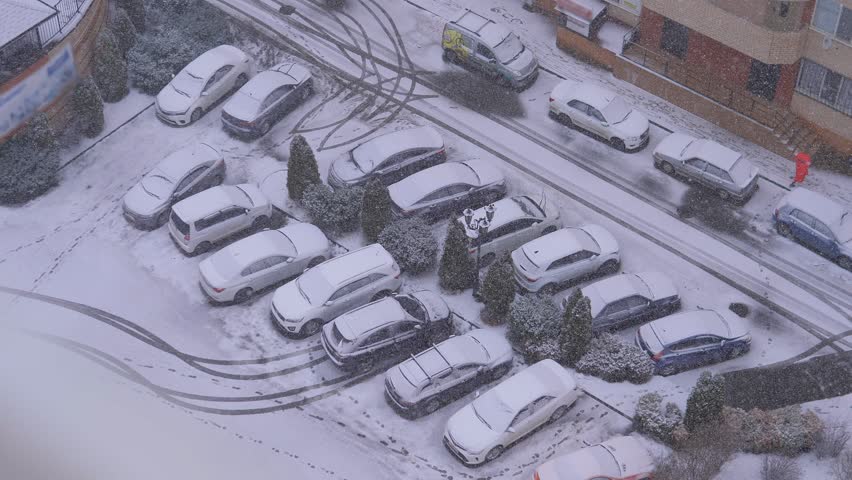 Heavy snowfall on city street, cars covered with white snow. Winter weather. Snowstorm in city, urban landscape. Snow falling in cold, frost day. Storm climate. Snowy road exterior. Buildings in ice.
