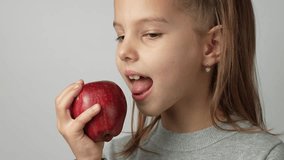 Cute girl eating apple. Child girl beats red apple, white background, 4k