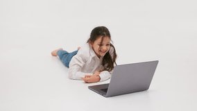 The concept of childish, sincere emotions. A little girl lies on the floor against a light background and watches a movie. Children's emotions from 