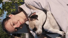 Beautiful girl holds a dog in her arms and strokes it. White-brown-black dog.  A cross between a Chihuahua and a Jack Russell dog. Vertical video