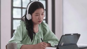 Young Asian university student women online lesson e-learning with digital tablet and headphones in the living room at home, remote education concept