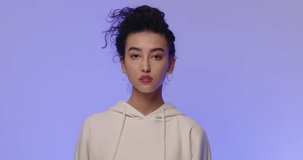 Portrait of young beautiful confident woman. Girl with Asian appearance in white hoodie on colored background. Beautiful curly hair tied in bun. Modern beauty, fashion trends, emotions and freedom