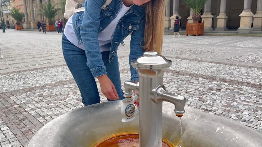 A beautiful girl fills a cup with healing mineral water in a natural hot spring in Karlovy Vary, Czech Republic.