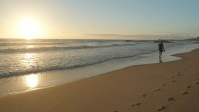 young man walking on a sandy ocean beach on a sunny summer day, in slow motion. Young Male guy walking along the sandy coast on a sunny evening. A guy with a backpack walks on a beach - Powered by Shutterstock - Get 15% off with code: PIKWIZARD15