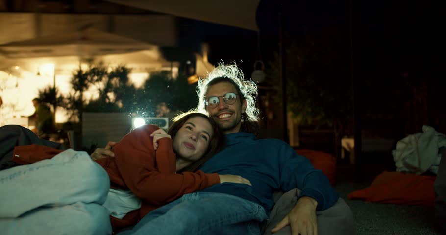 Close-up shot: a couple in love are lying on beanbag chairs and watching a movie. A party outside the city. Rest in the country house Royalty-Free Stock Footage #1110000289