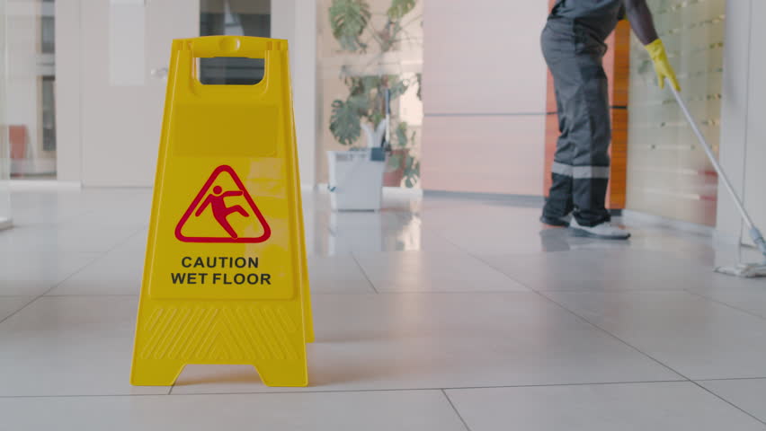 Cleaning Man Cleaning The Floor With Mop Inside An Office Building Behind A Wet Floor Warning Sign Royalty-Free Stock Footage #1110000535