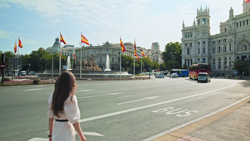 A girl tourist walking by the Cibeles Fountain in Madrid the Capital of Spain. A woman visiting the Neoclassical fountain depicting Cybele on a chariot pulled by 2 lions.