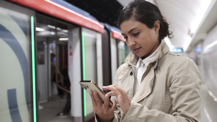 Happy woman standing at metro station. Girl using smartphone internet surfing, communication online. Female student holding phone checking news. Public transport. Browsing social networks site. 4K | Shutterstock HD Video #1110001973