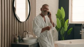 Happy smiling Caucasian retired elderly man talk smartphone friendly call make distant order speak cellphone senior mature old 60s male in bathroom in bathrobe talking mobile phone morning hygiene - Powered by Shutterstock - Get 15% off with code: PIKWIZARD15