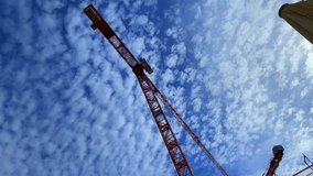 A crane against a background of blue sky with cirrus clouds. Construction crane, bottom view. 4K video shot with a wide-angle lens.