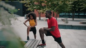 Beautiful african american couple stretching legs on wooden bench an at urban area. Smiling spouses in activewear training together outdoors for maintaining health and wellness. - Powered by Shutterstock - Get 15% off with code: PIKWIZARD15