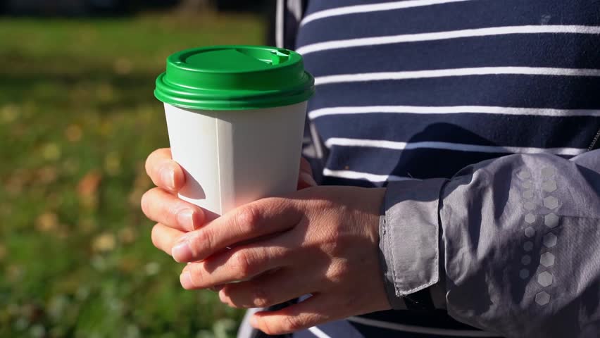 woman drinks hot coffee from a cup while walking in city on a sunny autumn day