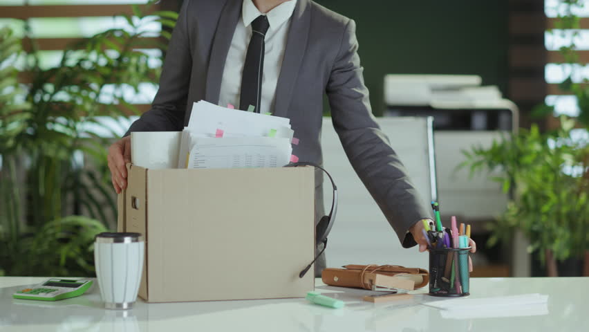 New job. Closeup on modern 40 years old woman worker in modern green office in grey business suit with personal belongings in cardboard box. Royalty-Free Stock Footage #1110016405